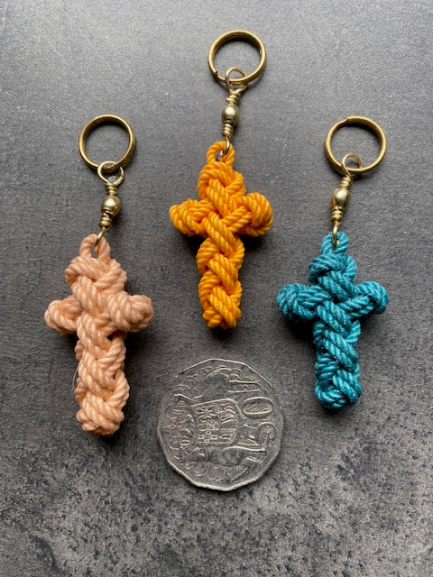 Three handmade Sailor’s Cross key fobs with brass-coloured rings and swivels beside a 50-cent coin